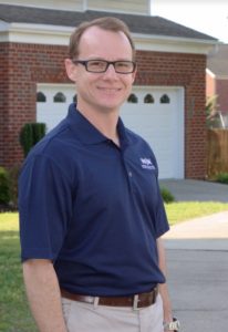 A WIN home inspector poses and smiles for a photo on the sidewalk in front of a garage.