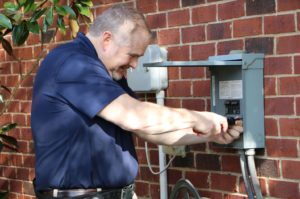 A WIN Home Inspection business owner inspects a fuse box on the outside of a brick home.