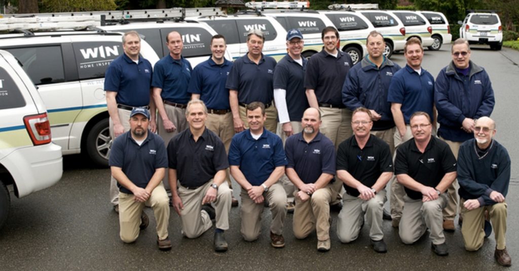 A group of WIN Strategic-Partners pose in front of a fleet of WIN Home Inspection vans.