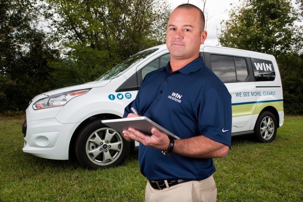 A WIN Strategic-Partner writes on a clipboard in front of a WIN Home Inspection van.
