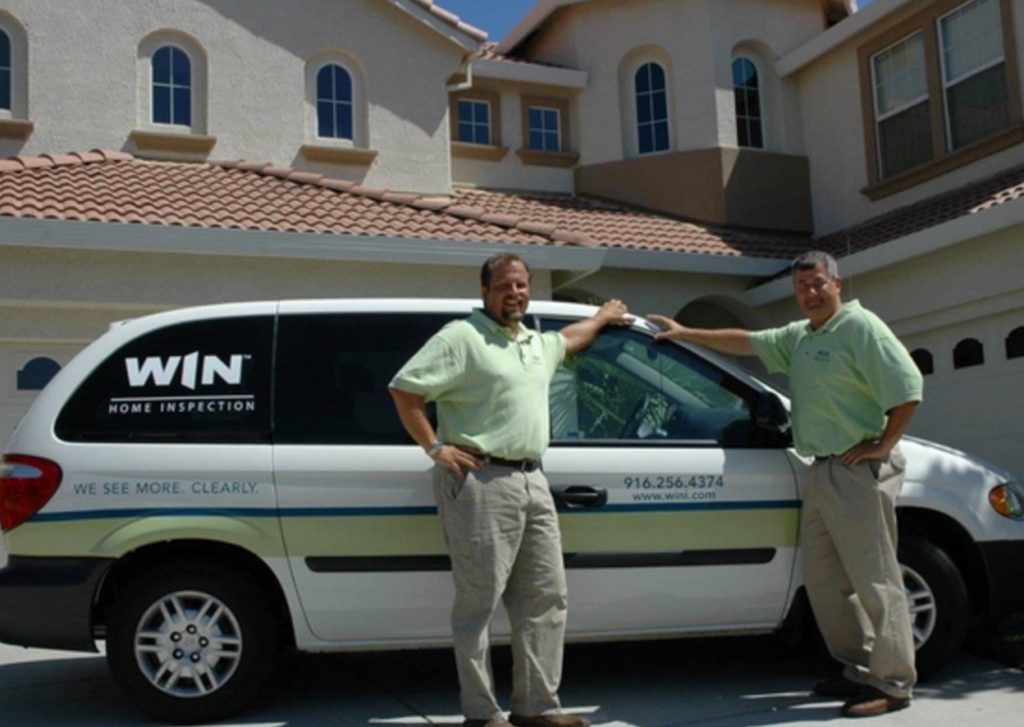 Two WIN Strategic-Partners stand with their hands on a WIN-branded van outside a home they’ve just inspected.