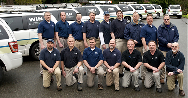 A group of 16 WIN Strategic-Partners, all dressed in dark blue polos and beige khaki pants, line up in front of their branded service vehicle minivans and SUVs.