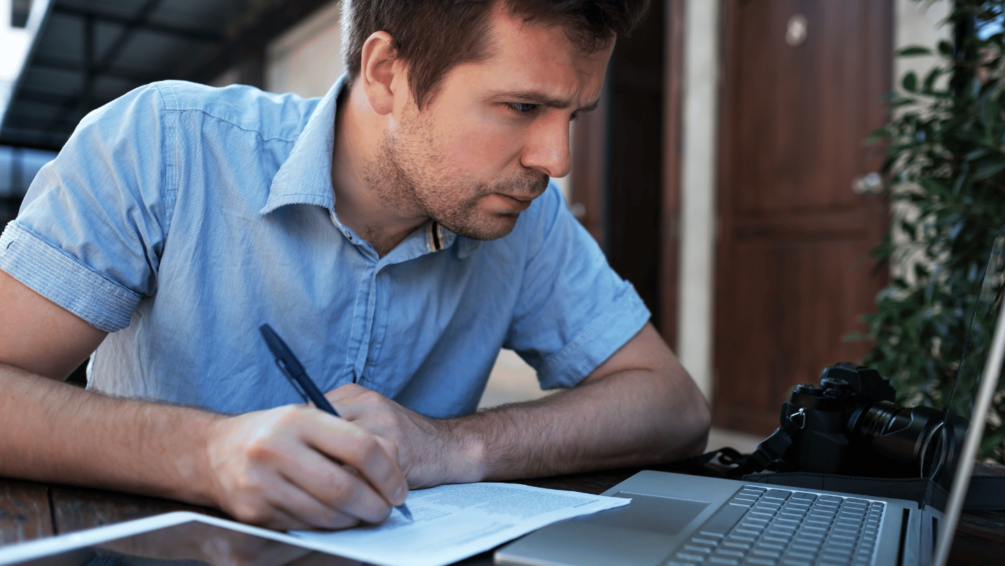 Man writing lean business plan on paper with a laptop in front of him.