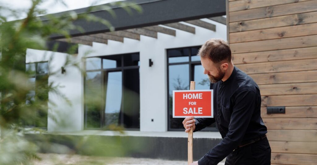Man placing a home for sale sign outside a modern house for real estate listing.